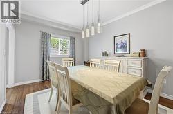 Dining area featuring wood-finish flooring, a contemporary linear chandelier, window treatments, and crown molding - 