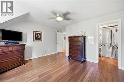 Spacious room featuring wood-finish flooring, a contemporary ceiling fan with integrated lighting, a bright white door, and an open closet with built-in shelving - 