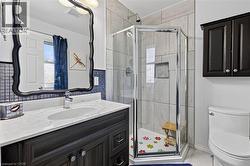 Bathroom featuring a corner glass-enclosed shower with tile surround, a dark wood-finish vanity with an undermount sink, a white countertop, and a decorative framed mirror - 