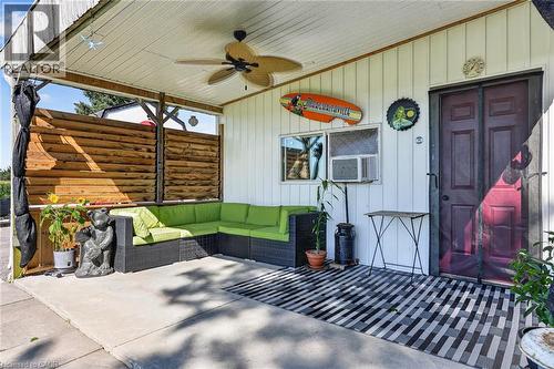 Covered patio featuring a ceiling fan, white paneled siding, a dark red door, and a horizontal wood-plank privacy wall - 184726 Cornell Road, Tillsonburg, ON - Outdoor With Exterior