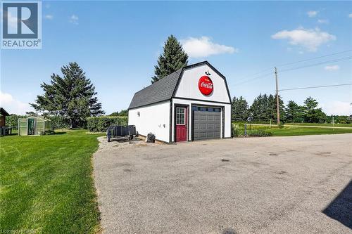 Detached garage structure with a gray overhead door and a red entry door - 184726 Cornell Road, Tillsonburg, ON - Outdoor