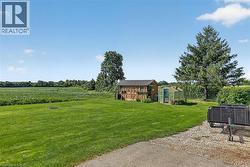 Spacious green lawn with a greenhouse, rustic outbuilding, mature trees, and agricultural fields in the background - 