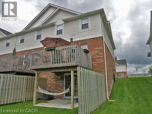 Rear exterior featuring a brick and siding facade, a raised wood deck, and a lower-level patio with a sliding glass door - 151 Clairfields Drive E Unit# 39, Guelph, ON - Outdoor With Exterior