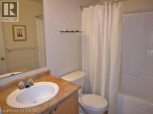 Bathroom featuring a wood-finish vanity with an oval basin sink, a light-toned countertop, a full-width wall mirror, and a white bathtub with an integrated shower - 151 Clairfields Drive E Unit# 39, Guelph, ON - Indoor Photo Showing Bathroom