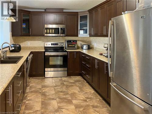 Kitchen featuring wood-finish cabinetry, light speckled countertops, and a tiled backsplash - 180 Huck Crescent, Kitchener, ON - Indoor Photo Showing Kitchen With Double Sink With Upgraded Kitchen