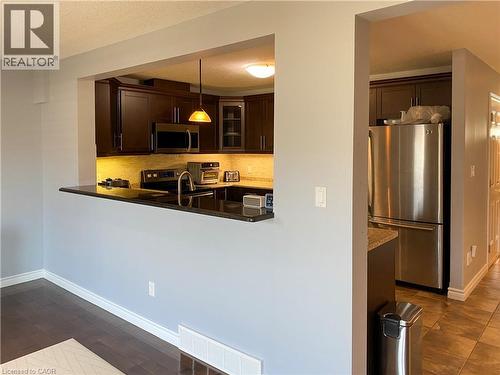 Kitchen featuring dark wood cabinetry, stainless steel appliances, black countertops, and under-cabinet lighting - 180 Huck Crescent, Kitchener, ON - Indoor Photo Showing Kitchen
