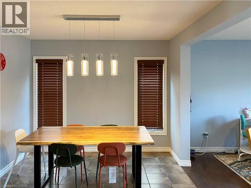 Dining area featuring a linear chandelier with four pendant lights, brown wood-finish blinds, light grey wall paint, and tile flooring - 180 Huck Crescent, Kitchener, ON - Indoor Photo Showing Dining Room