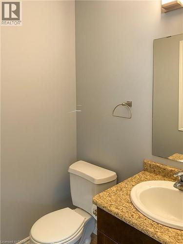 Powder room featuring a white toilet, dark wood-finish vanity with a granite-look countertop, and an undermount sink - 180 Huck Crescent, Kitchener, ON - Indoor Photo Showing Bathroom