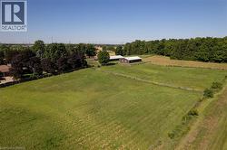Expansive green acreage featuring a large brown barn with a light-colored roof, multiple fenced paddocks, and mature tree lines bordering the property - 