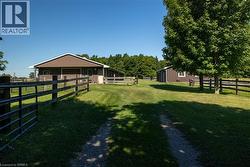 Gravel driveway leading to a brown barn structure with white trim, surrounded by wood fencing and verdant grounds - 