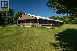 Expansive brown barn with a white metal roof, featuring multiple windows and a large sliding door, surrounded by a split-rail fence and green lawn - 