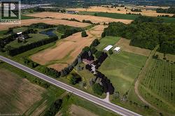 Expansive rural property featuring a main residence, cultivated fields, wooded areas, two white outbuildings, and a pond - 