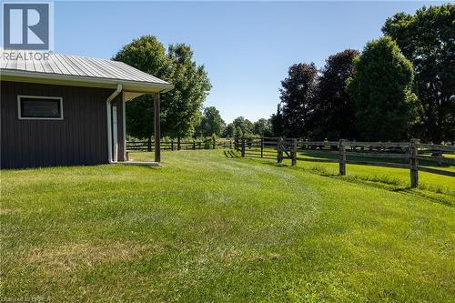 Expansive green lawn bordering a property structure with a metal roof and rain gutter system, featuring a fenced perimeter and mature trees - 269 Brant County Road 22, Ancaster, ON - Outdoor