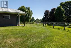 Expansive green lawn bordering a property structure with a metal roof and rain gutter system, featuring a fenced perimeter and mature trees - 