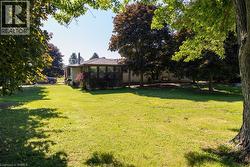 Expansive lawn area with mature trees and a single-story residence featuring a bay window extension - 