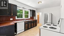 Kitchen featuring wood-finish countertops, black cabinetry, a double-basin sink, and a white dishwasher - 