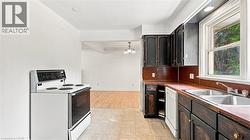 Kitchen featuring dark wood cabinetry, a white electric range, a double basin stainless steel sink, and a dishwasher - 