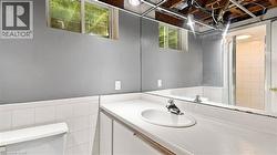 Bathroom featuring a spacious vanity with an integrated sink, large wall-mounted mirror, white ceramic wall tile, gray painted walls, and a shower with a glass enclosure - 