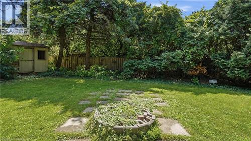 Expansive green lawn with mature perimeter trees, a wood storage shed, and a stone paver pathway leading to a circular garden bed - 524 Dorval Drive, Ancaster, ON - Outdoor
