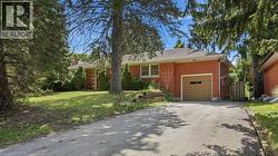 Brick-clad exterior featuring an attached garage, paved driveway, mature trees, and a front lawn - 