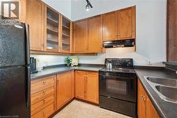 Kitchen featuring warm wood cabinetry, dark countertops, a black electric range, a stainless steel double sink, and a black refrigerator - 