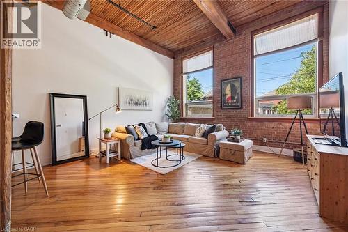 Spacious living area featuring exposed brick walls, wood-finish flooring, and an exposed wood-beam ceiling - 26 Ontario Street Unit# 127, Guelph, ON - Indoor