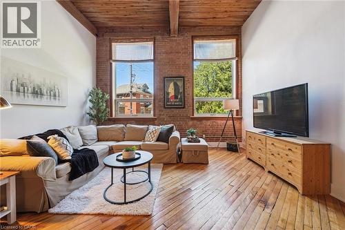 Living area featuring exposed brick walls, high ceilings with exposed wood beams, and wide plank wood-finish flooring - 26 Ontario Street Unit# 127, Guelph, ON - Indoor Photo Showing Living Room