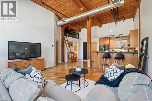 Open-concept living space featuring high vaulted ceilings, exposed wood beams, wood-finish flooring, a kitchen island with seating, and a prominent lofted area accessed by a ladder - 26 Ontario Street Unit# 127, Guelph, ON - Indoor Photo Showing Living Room