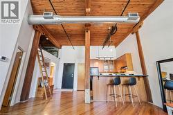 Open-concept living area featuring a wood-plank ceiling, exposed wood beams, and a large industrial-style duct - 