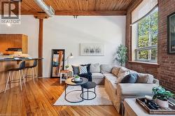 Open-concept living area featuring exposed brick walls, wood-finish flooring, and a natural wood-plank ceiling with exposed beams - 