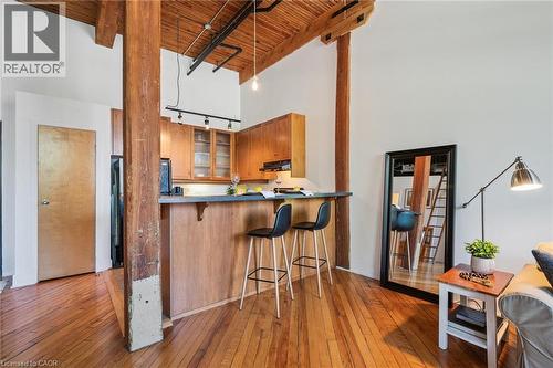 Open-concept living space featuring wood-finish flooring, exposed wooden beams, and a wood-paneled breakfast bar - 26 Ontario Street Unit# 127, Guelph, ON - Indoor