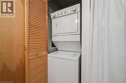 White stackable washer and dryer unit, featuring a top-loading washer and front-loading dryer, encased by louvered bi-fold doors with a wood-finish - 