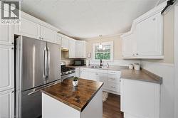 Bright kitchen featuring white cabinetry, stainless steel appliances, a center island with a wood-finish countertop, and a window above the sink - 