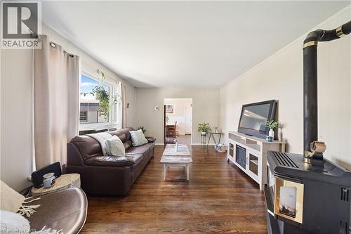 Living area featuring wood-finish flooring, a large window with white trim, and a black freestanding stove with a visible flue - 3 Bousfield Lane, Jarvis, ON - Indoor Photo Showing Living Room