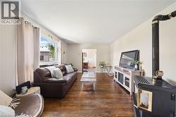 Living area featuring wood-finish flooring, a large window with white trim, and a black freestanding stove with a visible flue - 