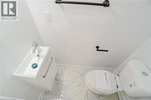 Bathroom featuring a wall-mounted vanity with integrated sink, chrome faucet, white toilet, and marbled floor tile - 8 Marlborough Road, Guelph, ON - 