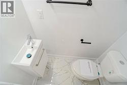 Bathroom featuring a wall-mounted vanity with integrated sink, chrome faucet, white toilet, and marbled floor tile - 
