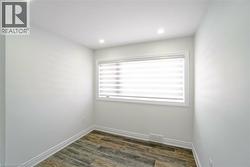 Neutral-toned room featuring wood-finish flooring, recessed lighting, and a window with horizontal blinds - 