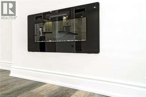 Wall-mounted electric fireplace with a black glass front and decorative white stones, complemented by light wood-finish flooring and white baseboards - 8 Marlborough Road, Guelph, ON - Other