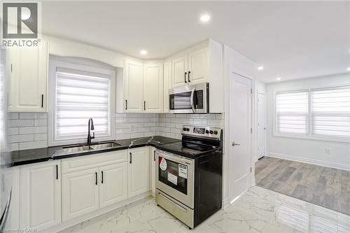 Kitchen featuring white shaker-style cabinetry with black hardware, dark countertops, a subway tile backsplash, and stainless steel appliances - 8 Marlborough Road, Guelph, ON - Indoor Photo Showing Kitchen With Double Sink With Upgraded Kitchen