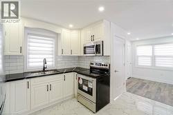 Kitchen featuring white shaker-style cabinetry with black hardware, dark countertops, a subway tile backsplash, and stainless steel appliances - 
