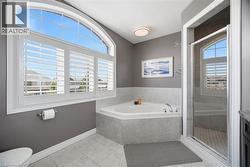 Bathroom with corner soaking tub, glass-enclosed shower, and a large arched window featuring white plantation shutters - 