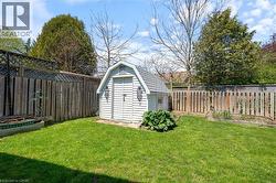 Fenced backyard featuring a white storage shed with barn-style roofing, a raised garden bed, and mature perimeter trees - 