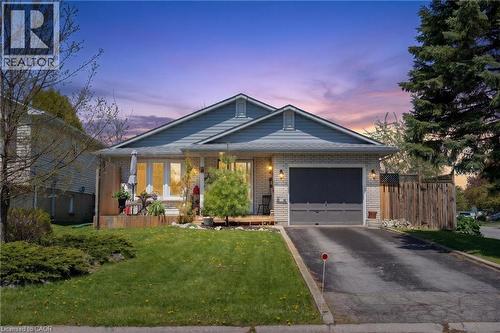Brick and siding exterior featuring an attached garage with a dark gray door, a paved driveway, a front yard with manicured lawn and shrubs, and a raised wooden deck - 2 Hampton Court, Port Dover, ON - Outdoor