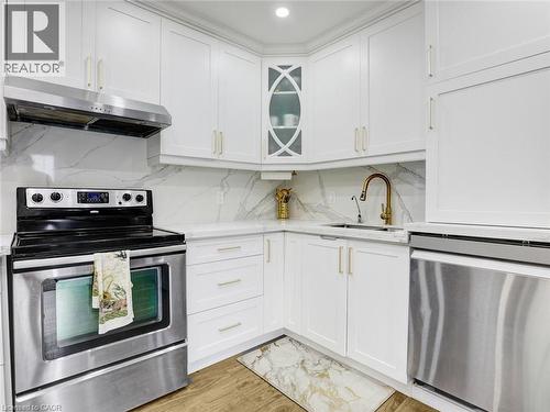 Contemporary kitchen featuring white cabinetry with gold-tone hardware, a stainless steel range and hood, a corner sink with a brass faucet, and white countertops complemented by a matching backsplash - 209 Briarmeadow Drive, Kitchener, ON - Indoor Photo Showing Kitchen With Upgraded Kitchen