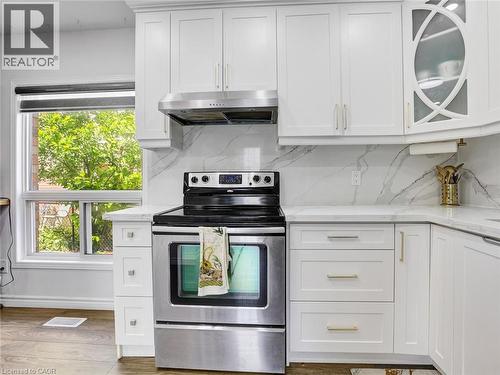 Modern kitchen featuring white shaker-style cabinetry, stainless steel oven with range hood, light-toned countertops, and a full-height backsplash with a marble-effect pattern - 209 Briarmeadow Drive, Kitchener, ON - Indoor Photo Showing Kitchen With Upgraded Kitchen