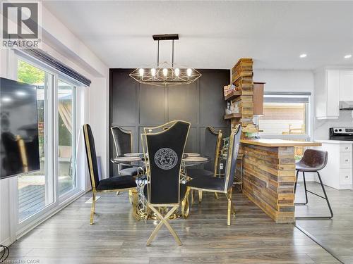 Open-concept dining area featuring wood-finish flooring, a contemporary chandelier, a contrasting paneled accent wall, a sliding glass door, and a breakfast bar with built-in shelving - 209 Briarmeadow Drive, Kitchener, ON - Indoor
