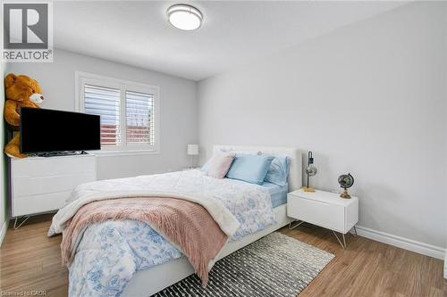 Bright bedroom featuring a window with white shutters, wood-finish flooring, light grey walls, and a ceiling-mounted light fixture - 209 Briarmeadow Drive, Kitchener, ON - Indoor Photo Showing Bedroom