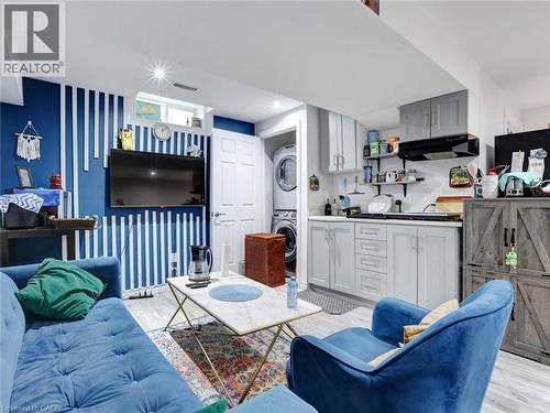 Integrated laundry area with stacked appliances, compact kitchenette featuring light gray cabinetry and a range hood, and light-tone wood-finish flooring - 209 Briarmeadow Drive, Kitchener, ON - 