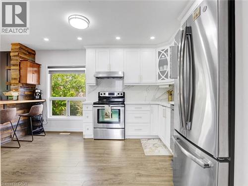 Modern kitchen featuring white cabinetry, stainless steel appliances, wood-finish flooring, recessed lighting, and a window with exterior views - 209 Briarmeadow Drive, Kitchener, ON - Indoor Photo Showing Kitchen